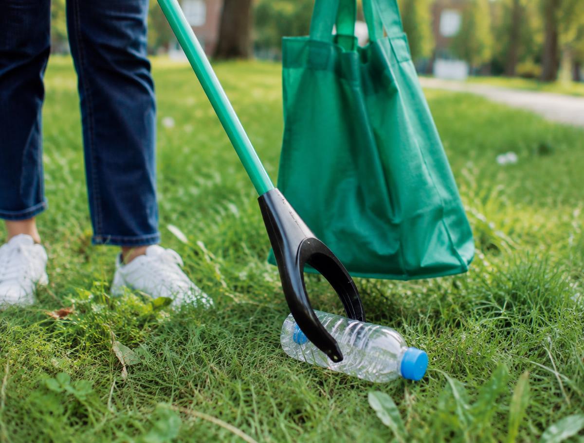 Volunteer using a green-handled litter grabber to pick up a plastic bottle from park grass